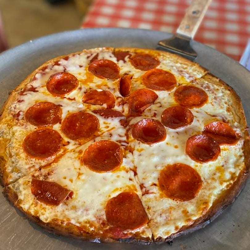 A whole pepperoni pizza with melted cheese and a pizza server on a metal pan.
