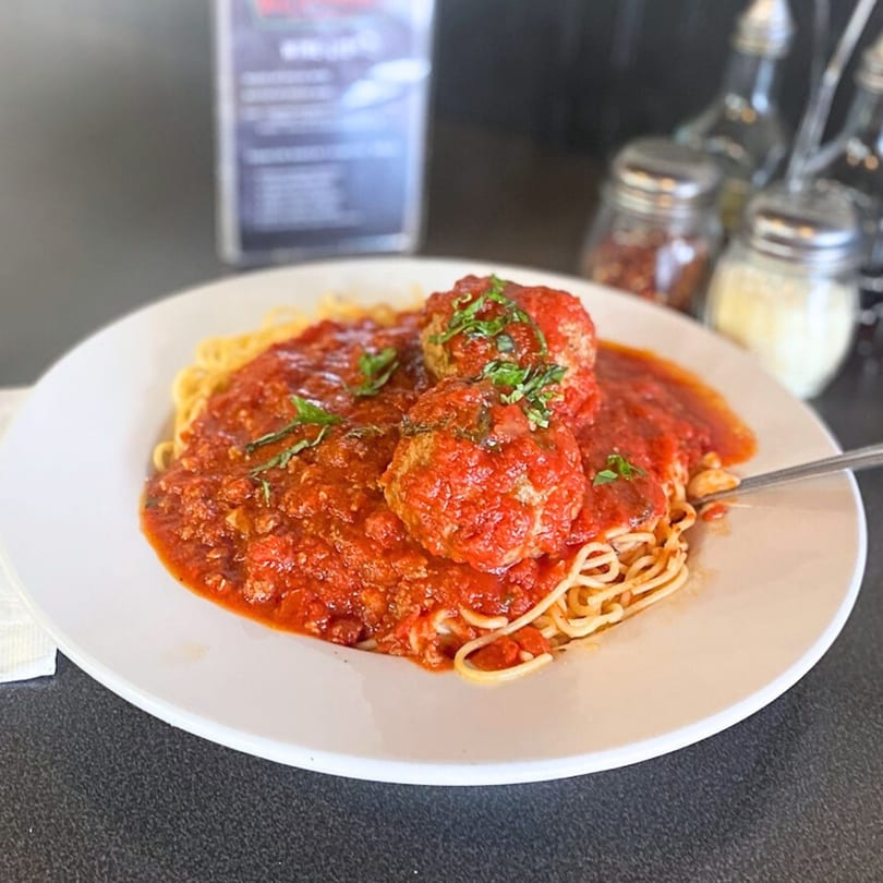 Spaghetti with meatballs and rich red sauce, garnished with fresh herbs, on a white plate.